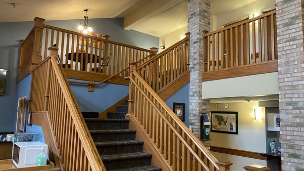 A multi-level wooden staircase with a chandelier, a brick column, and a coffee machine on the lower level.