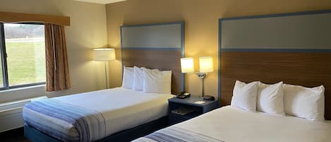 A hotel room with two beds, each with a striped bedspread, a nightstand with a lamp, and a window with curtains.