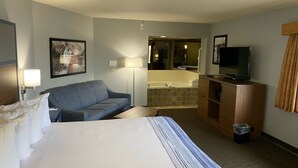 A hotel room with a large bed, a sofa, a TV, a desk, and a bathroom visible through an open door.