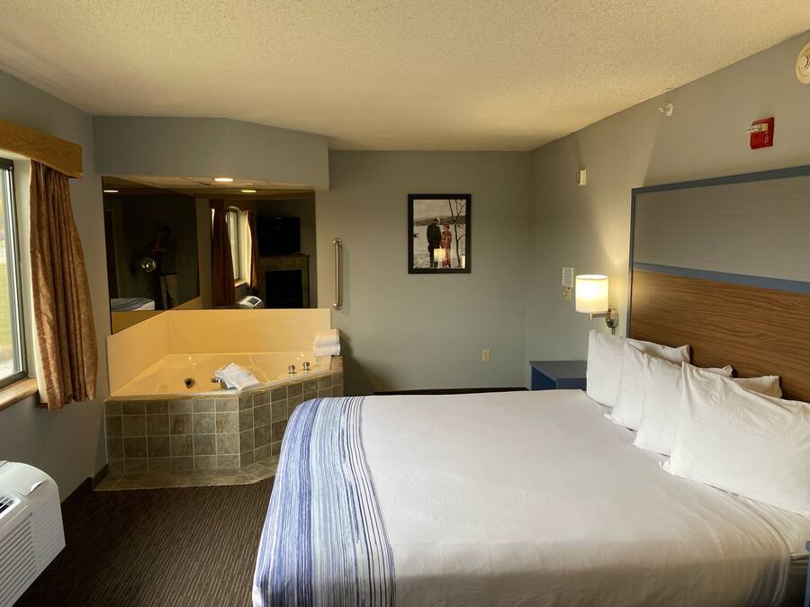 A hotel room with a large bed, a bathroom with a bathtub, a mirror, and a picture on the wall.