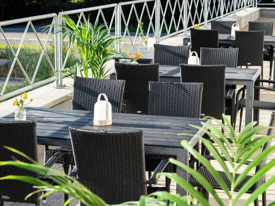 An outdoor seating area with black wicker tables and chairs, a potted plant, and a white handbag on one of the tables.