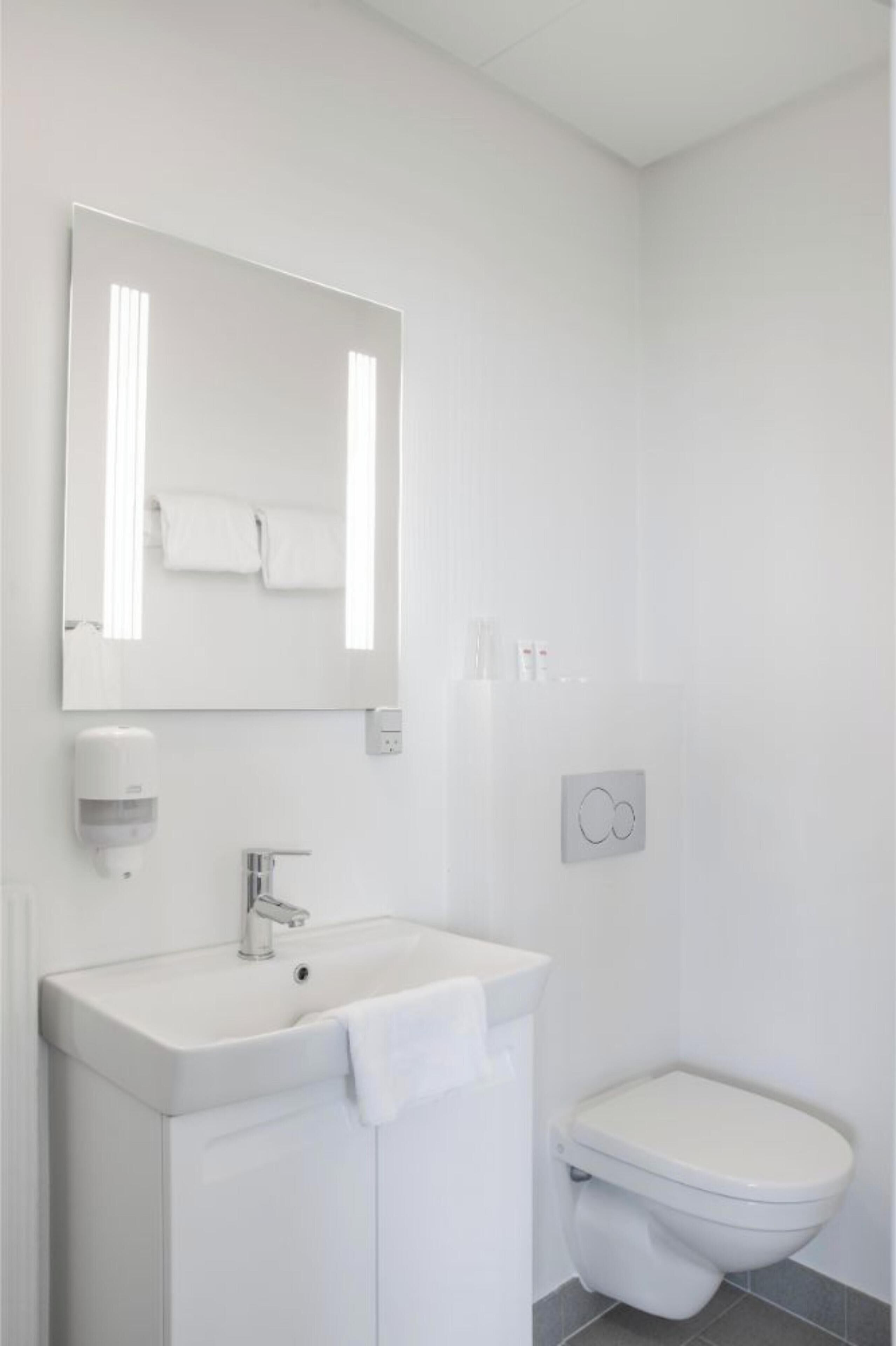 Ein modernes Badezimmer mit Waschbecken, Spiegel und Toilette in Weiß.