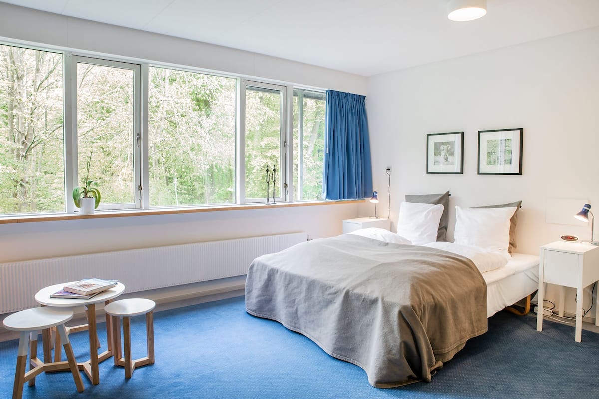 A bedroom with a bed, bedside tables, a small round table, and a window with curtains.