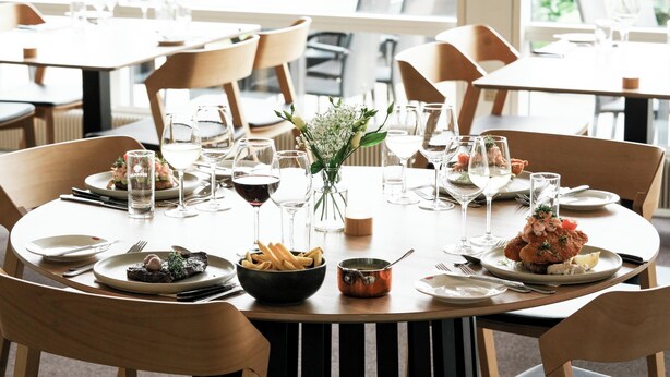 A dining table set with plates, glasses, and a vase of flowers.