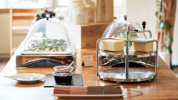 A breakfast buffet setup with a variety of food items, including a cake on a stand, a glass container with a lid, and a small bowl with a spoon.