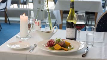 A dining table set with a candle, a bottle of wine, a glass of water, and a plate of food.