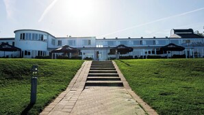 A large, white building with a central staircase leading to a door, surrounded by well-maintained grass and a paved walkway.