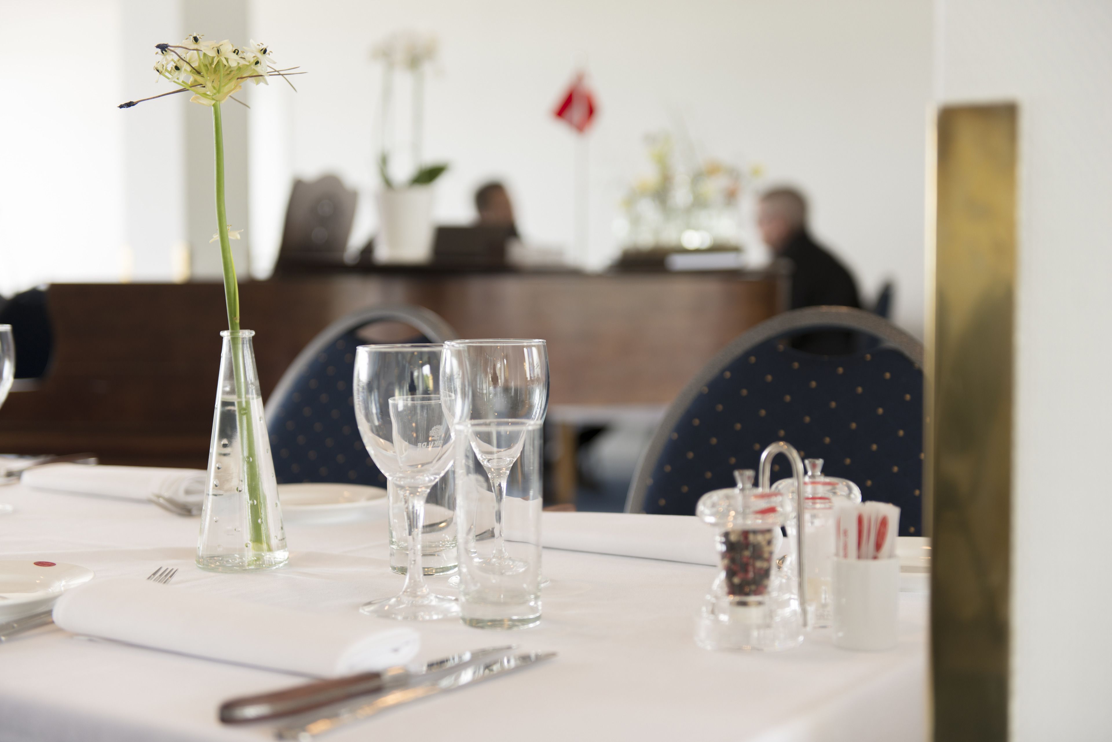 Una mesa de comedor dispuesta con cristalería transparente, un florero con una sola flor y un salero y pimentero.