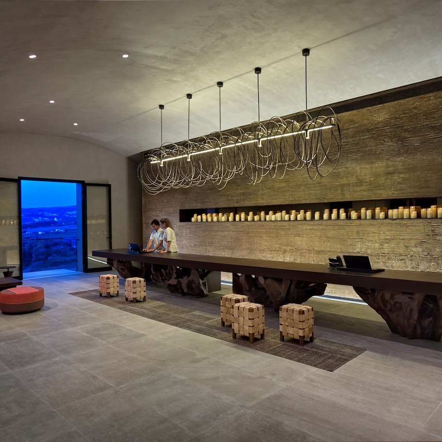 A modern interior with a long wooden table, red cushioned seating, and a view of a cityscape through a glass door.