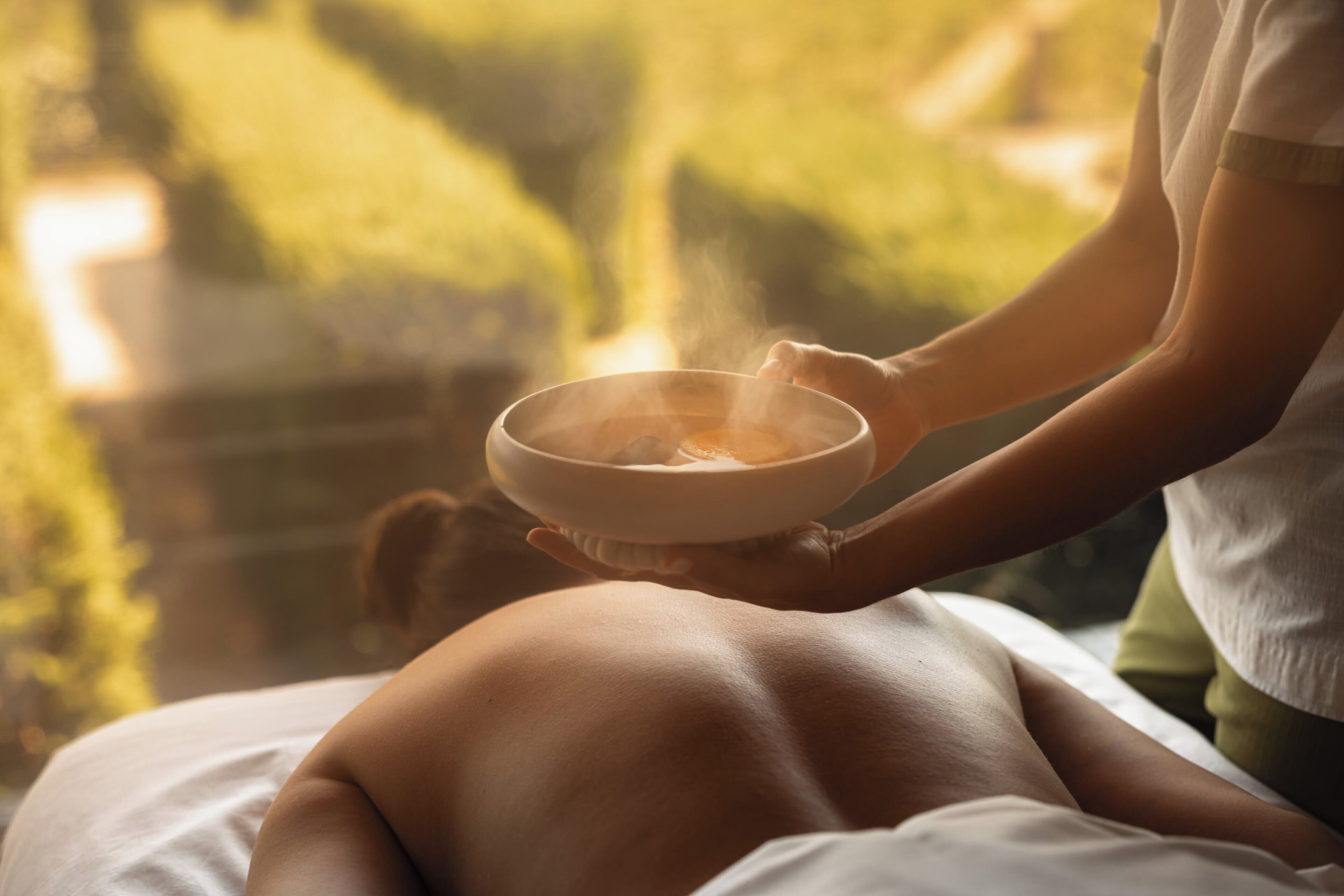 A person receiving a hot stone massage with a bowl of hot stones.