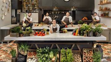 A kitchen with a central island stocked with fresh produce, a clock on the wall, and hanging pots.