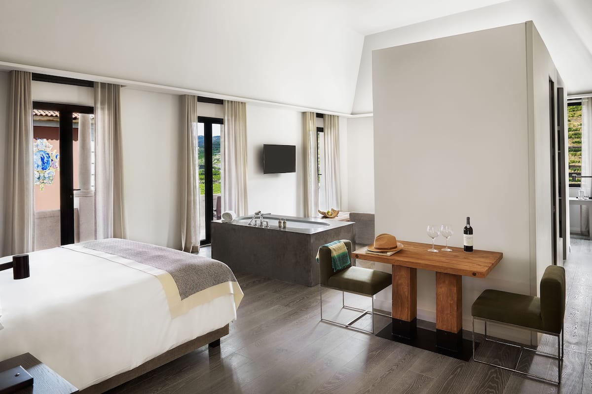 Ett modernt hotellrum med en stor säng, ett matbord i trä, en liten sittgrupp, ett inbyggt badkar och en platt-TV.
