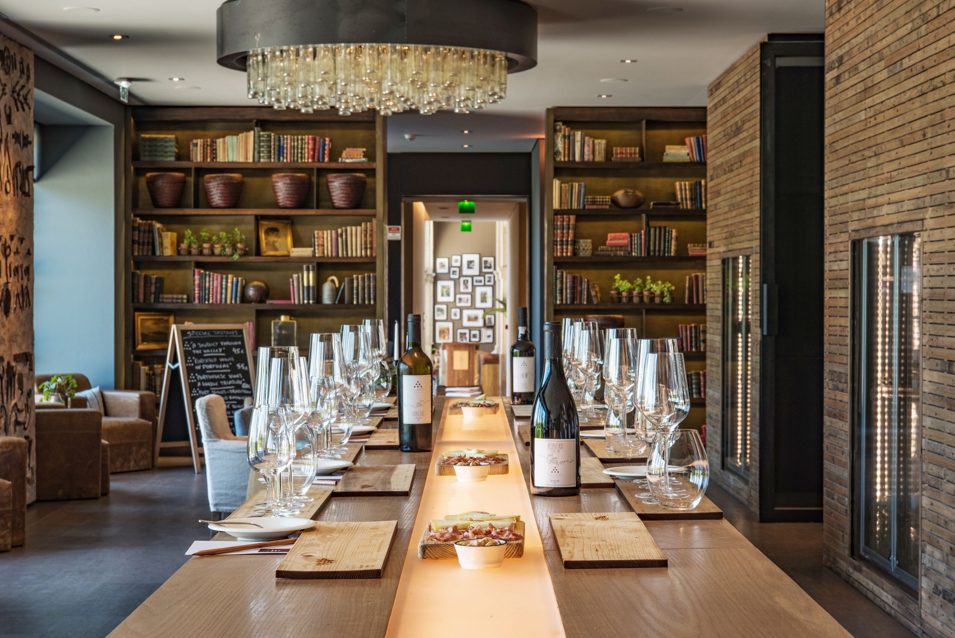 Una larga mesa con copas de vino y botellas, rodeada de estanterías y un candelabro.