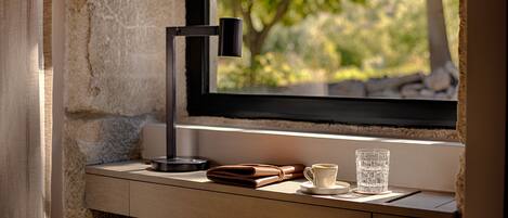 Un escritorio con una computadora portátil, una billetera, una taza y un vaso, ubicado junto a una ventana con vistas a árboles.
