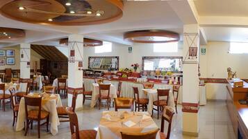 Um restaurante com várias mesas e cadeiras, um espaço de bar e uma parede de pedra ao fundo.