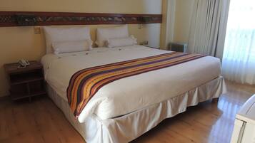 Una cama grande con una manta a rayas, cabecera de madera, mesita de noche con teléfono y ventana con cortinas.