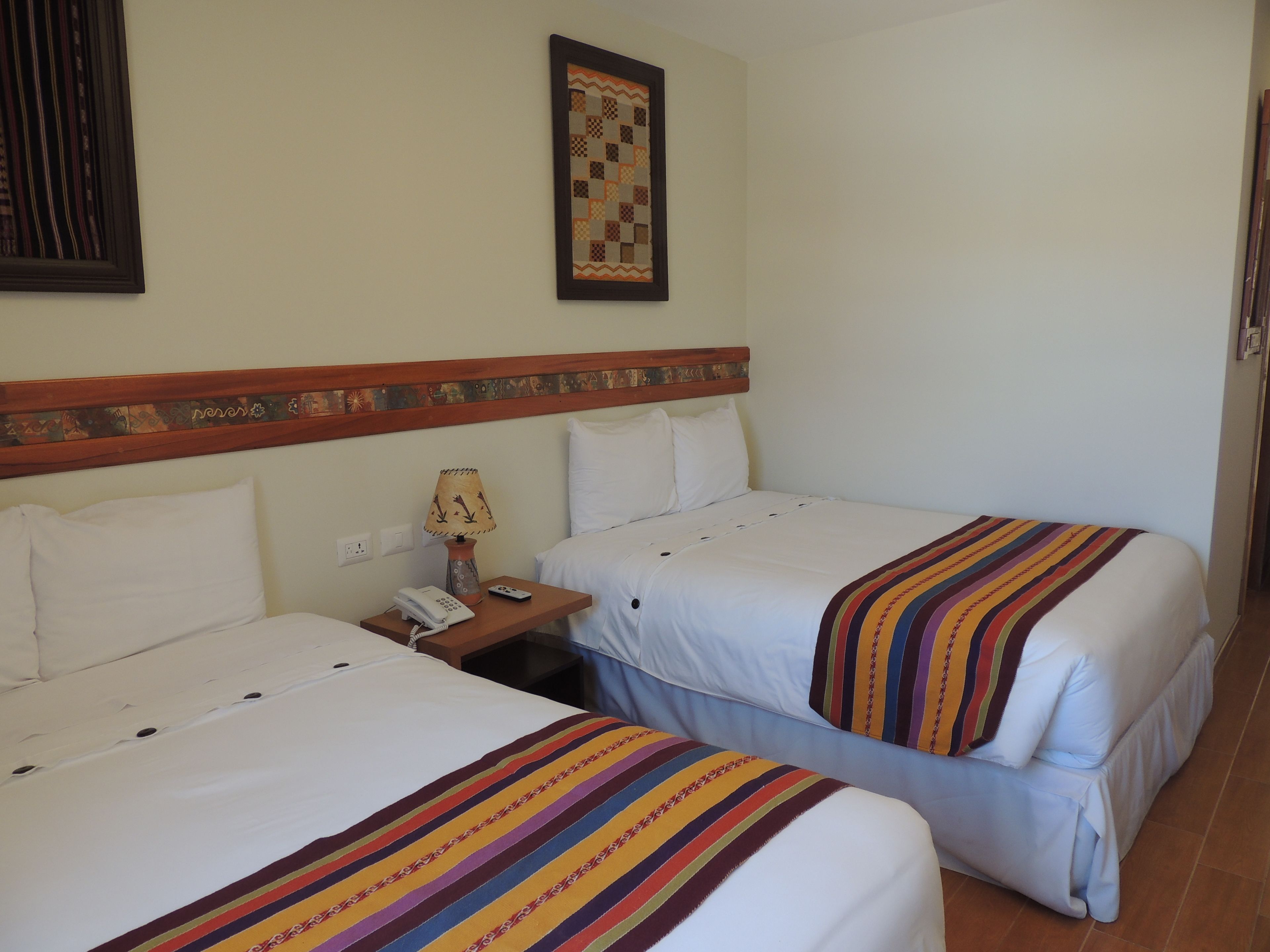 Une chambre d’hôtel avec deux lits, une table de chevet avec une lampe, un téléphone et un élément décoratif mural.
