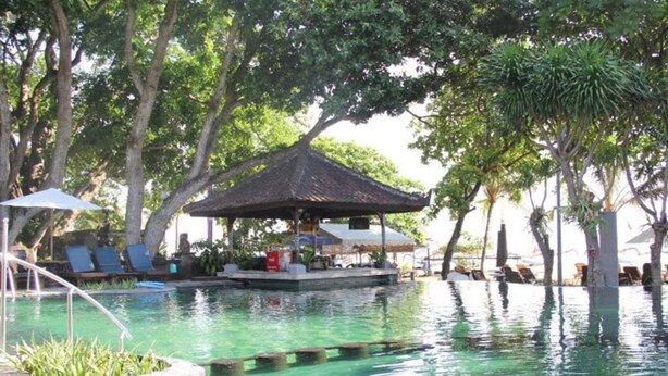 A pool area with lounge chairs and a shaded seating area. - Besakih Beach Hotel (Denpasar)