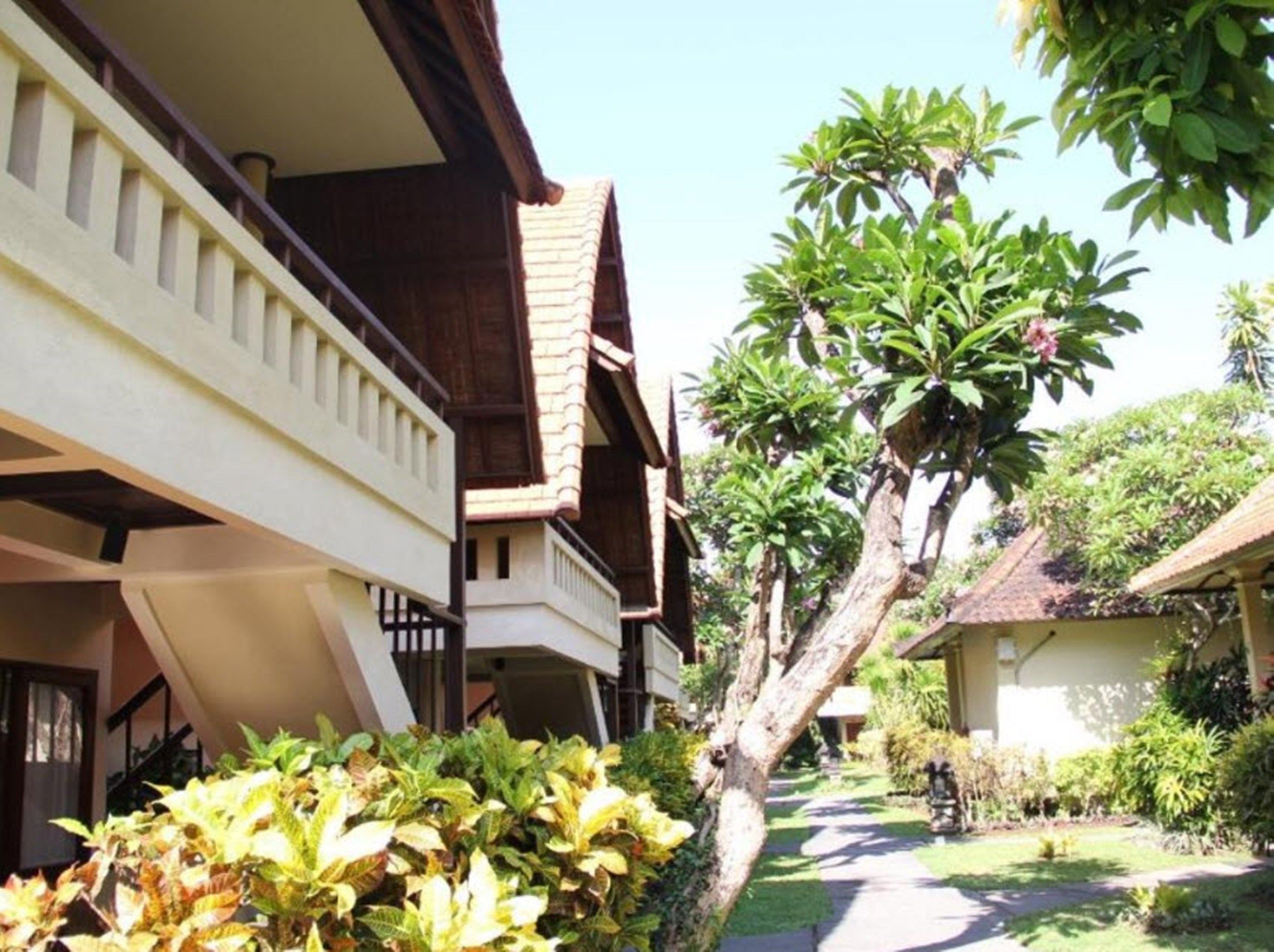 A traditional wooden building with a balcony, surrounded by lush greenery and a clear sky.