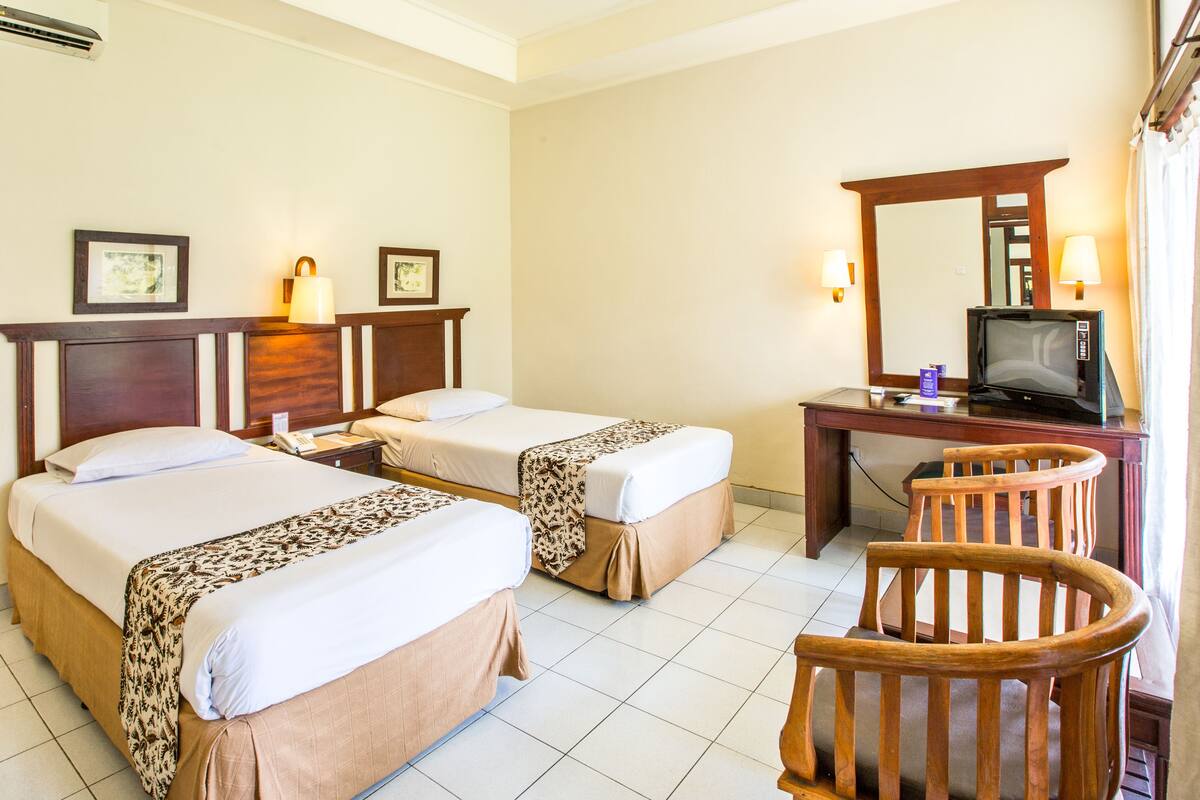 A hotel room with two beds, a desk with a television, and a chair.