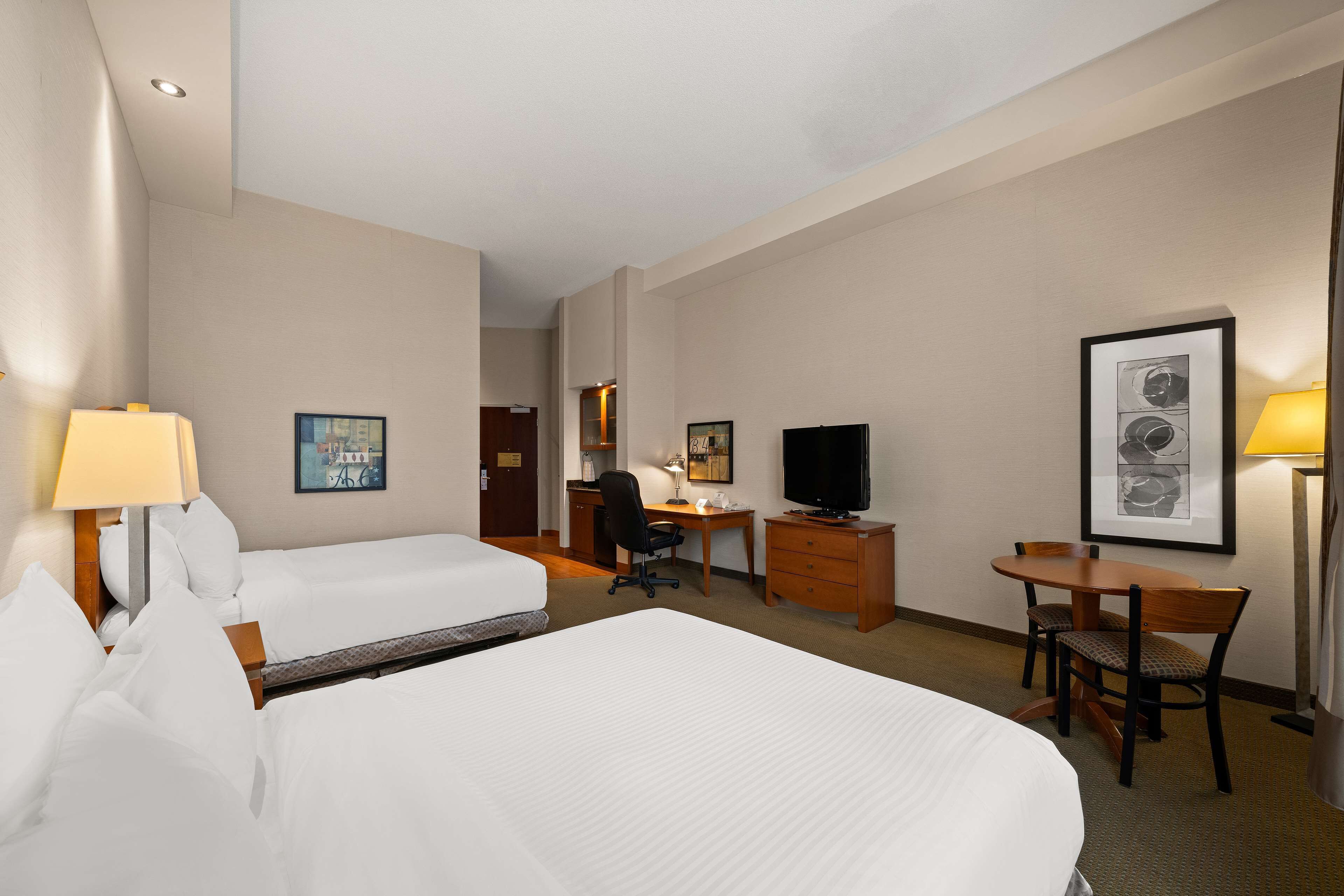 A hotel room with two beds, a desk, a chair, a television, and a small table with chairs.