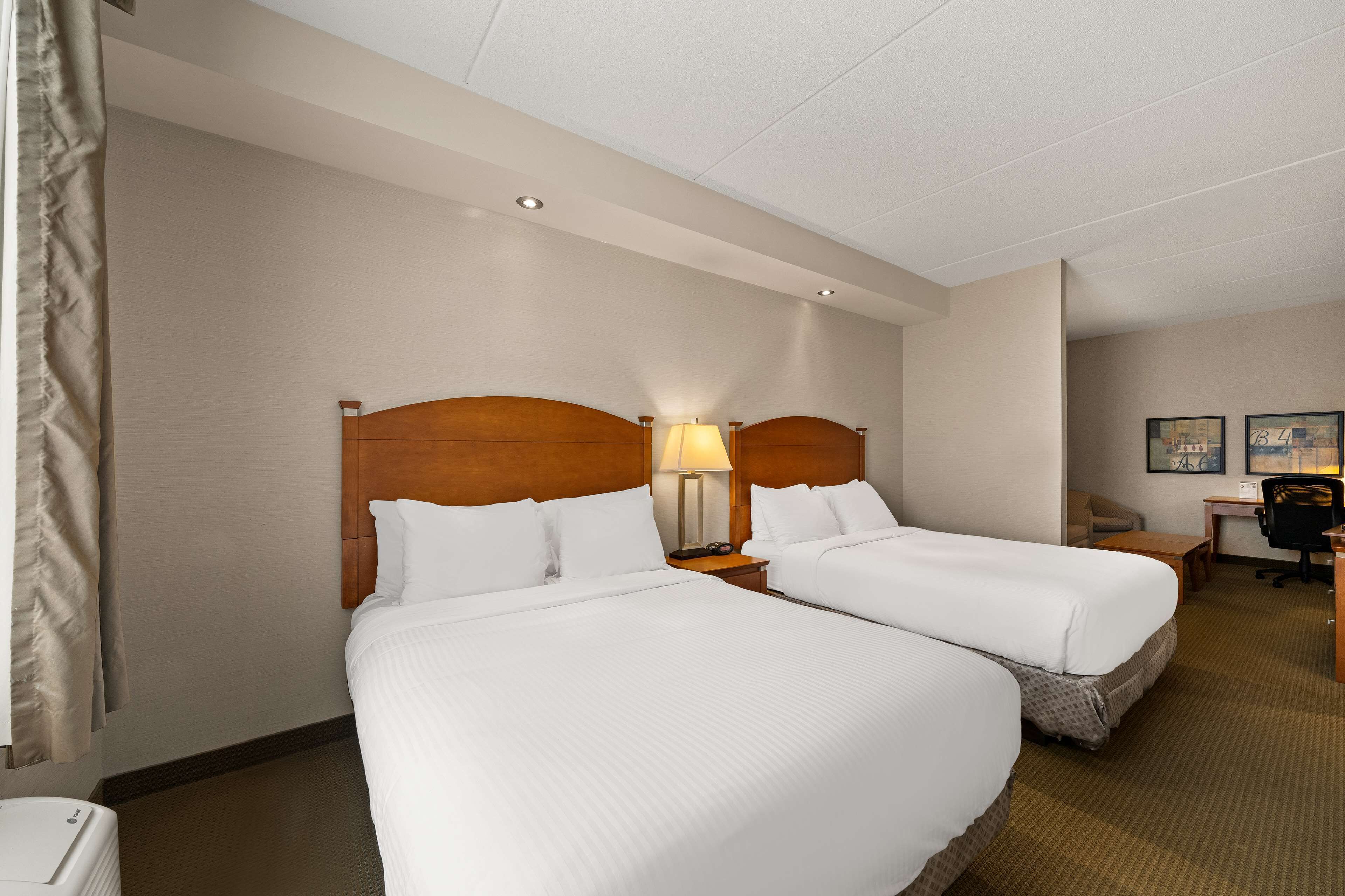 Habitación de hotel con dos camas, un escritorio, una silla y una lámpara.