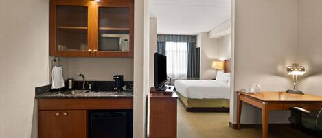 Une chambre d’hôtel équipée d’une kitchenette, d’un lit, d’un bureau et d’une télévision.