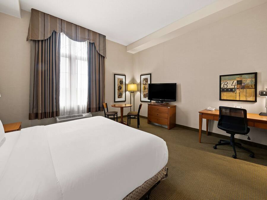 A hotel room with a large bed, a desk with a computer, a TV, and a small table with chairs.