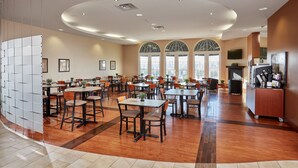 Un comedor amplio con múltiples mesas y sillas, ventanas grandes con arcos y un diseño de techo moderno.