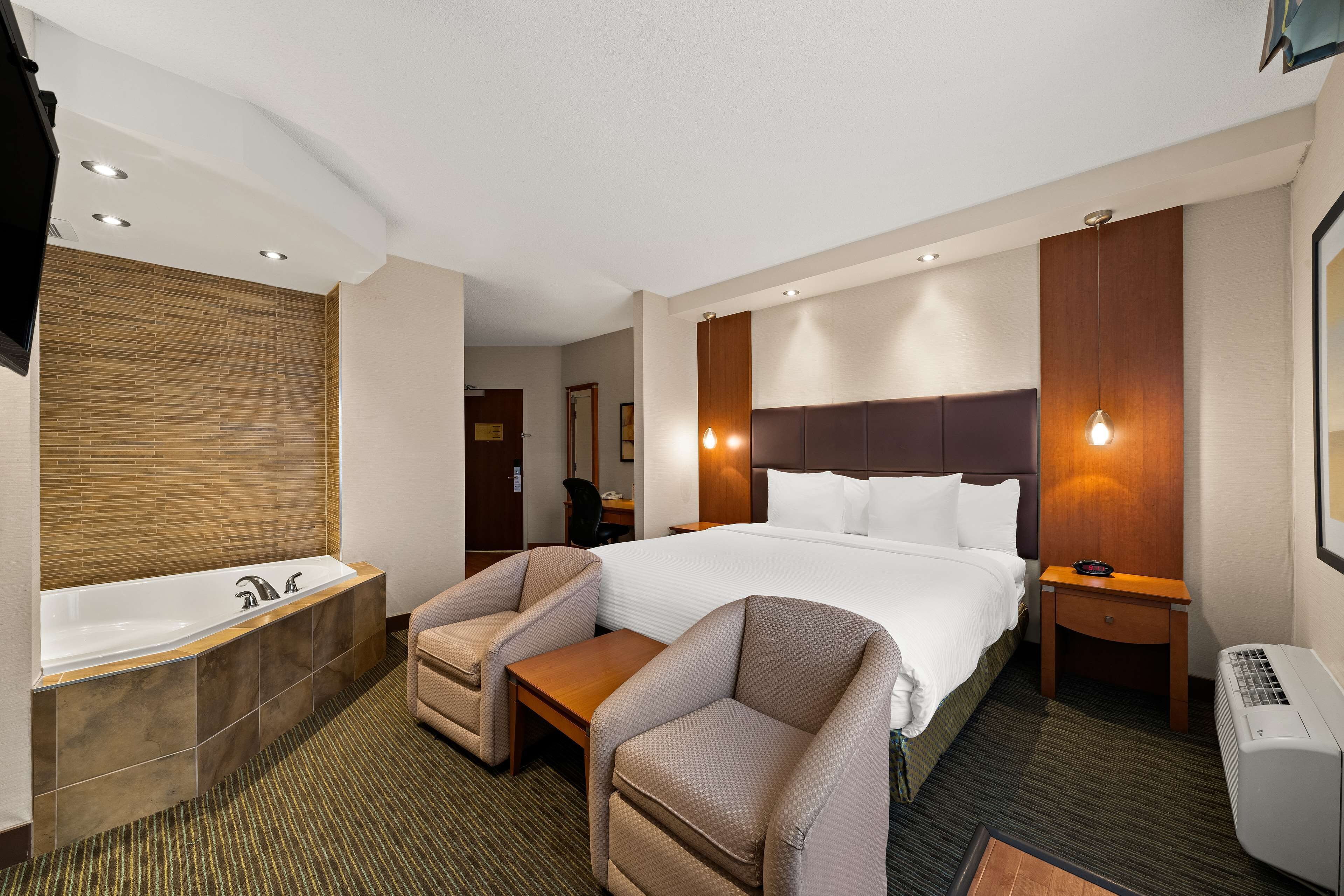 A hotel room with a large bed, a separate seating area, a bathtub, and a desk.