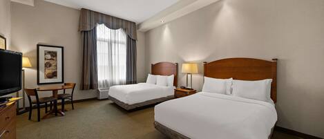 A hotel room with two beds, a desk, a chair, a TV, and a window with curtains.