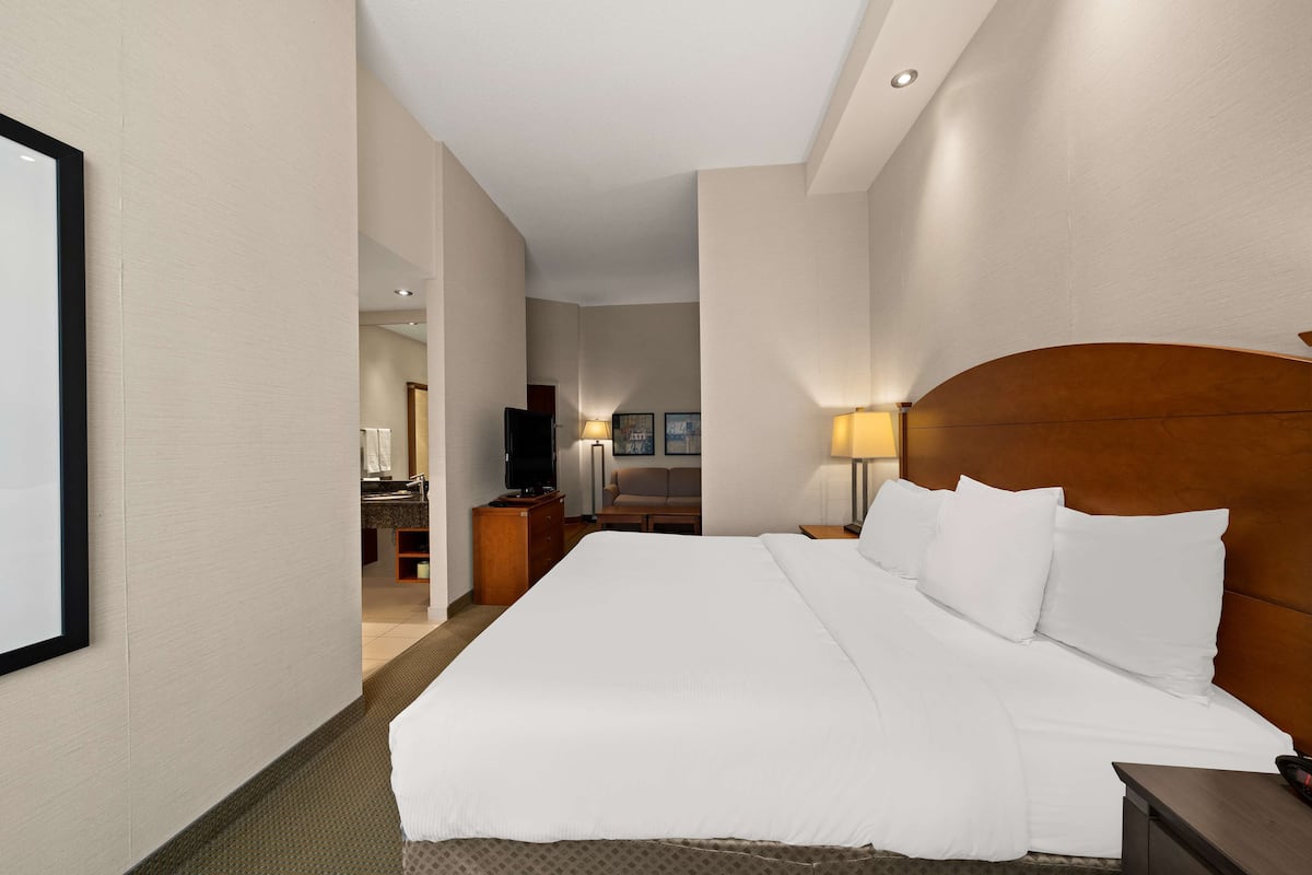A hotel room with a large bed, a wooden headboard, a bedside table, and a lamp.