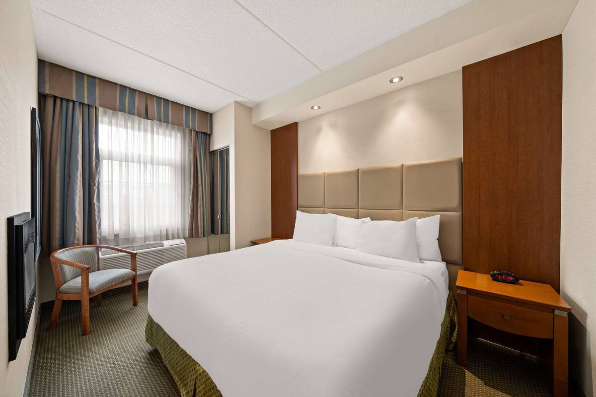 A hotel room with a large bed, a wooden chair, a desk, and a television.