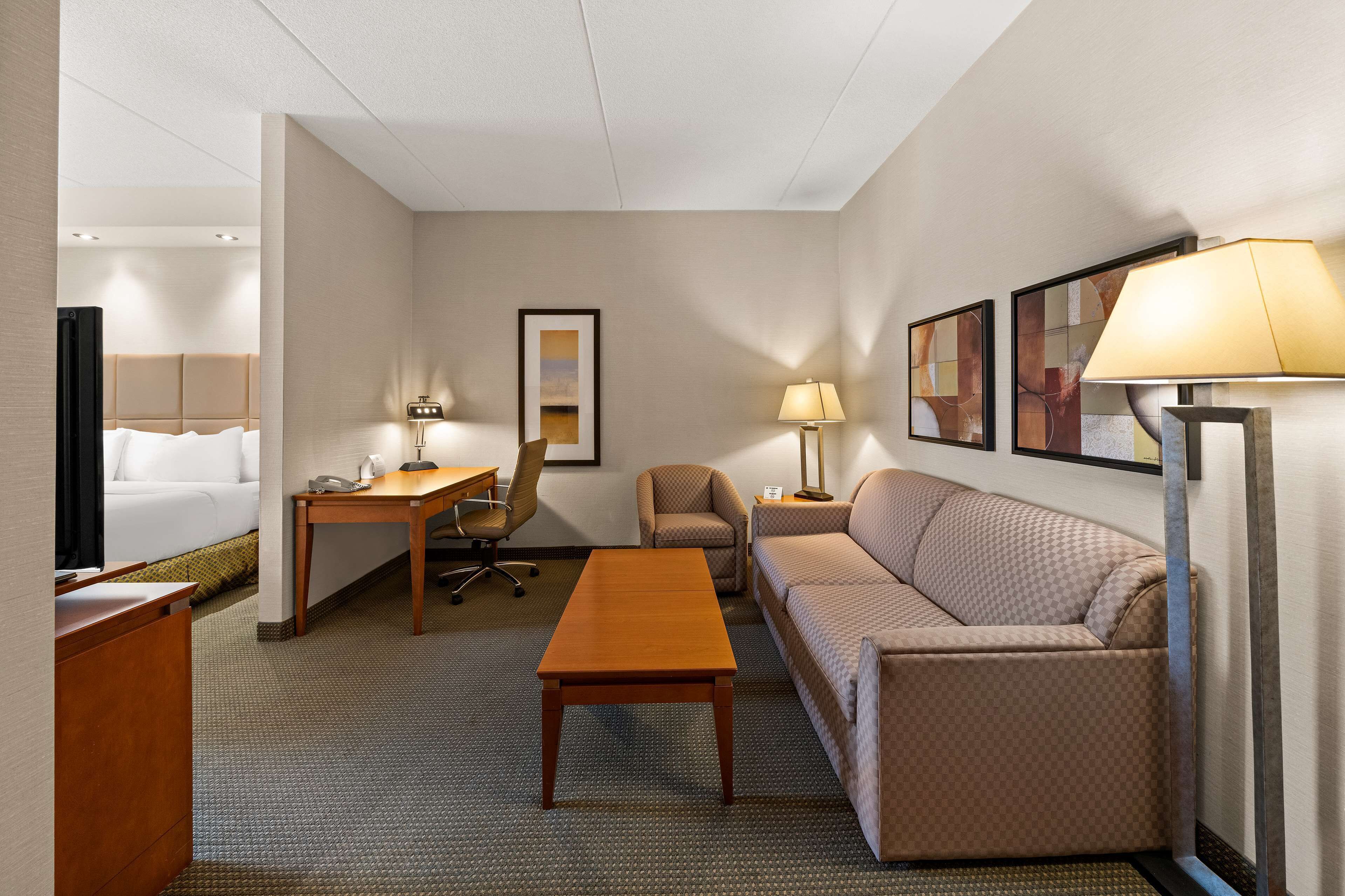 Quarto de hotel com cama, escrivaninha, cadeira, sofá e mesa de centro.