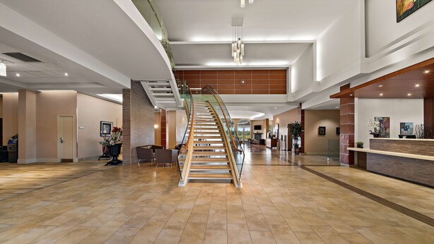 Un vestíbulo amplio con una escalera central, un mostrador de recepción y un candelabro moderno.
