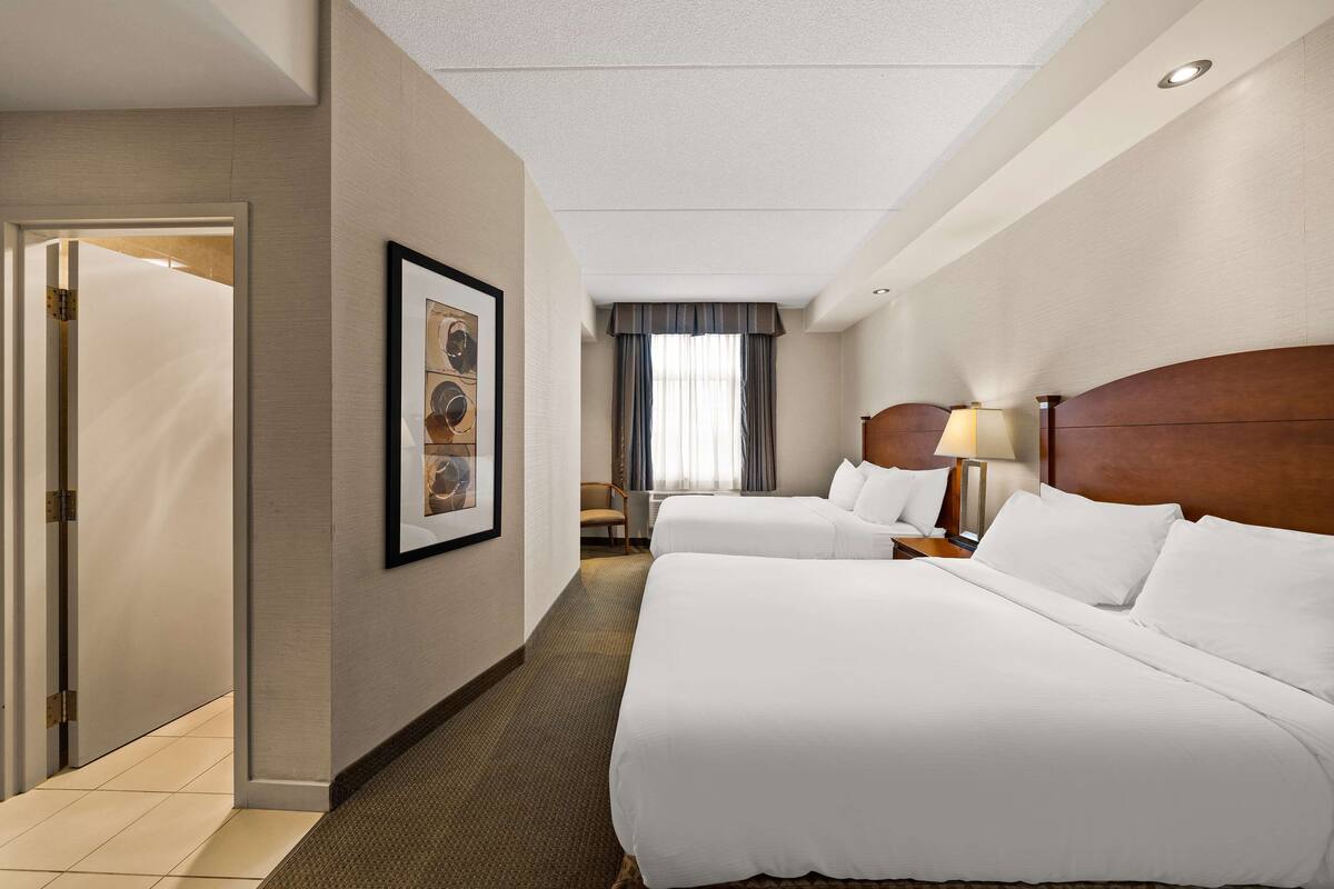A hotel room with two beds, a desk, a chair, and a window with curtains.