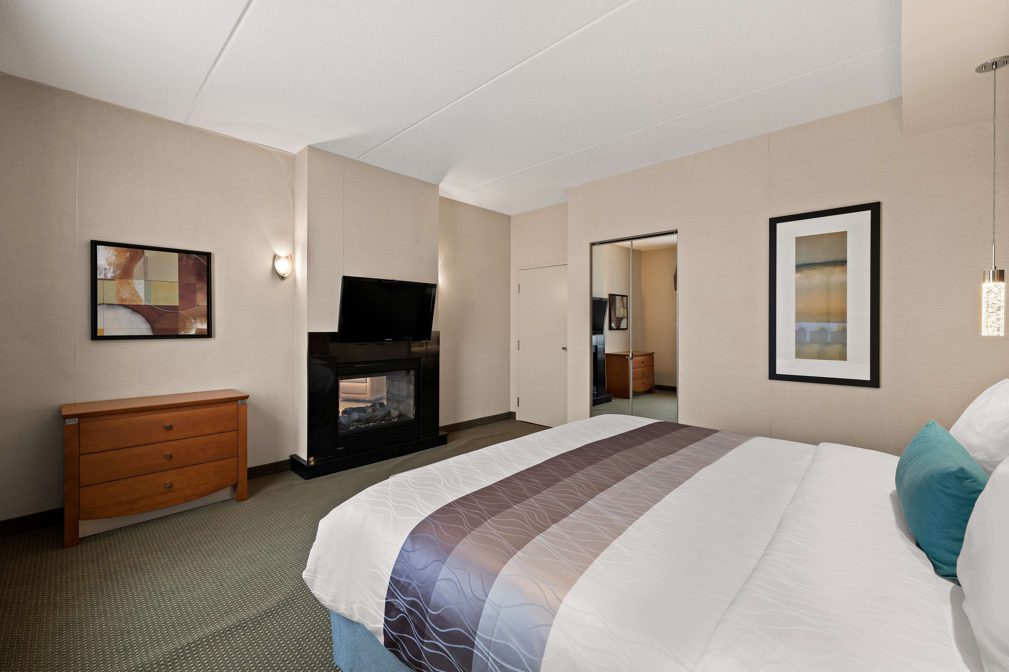 A hotel room with a large bed, a wooden dresser, a flat-screen TV, and a fireplace.