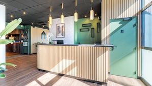 A reception desk with vertical wooden slats, pendant lighting, framed artwork, and a green door. - Campanile PRIME - Lyon Meyzieu Eurexpo Arena Stadium (Meyzieu)