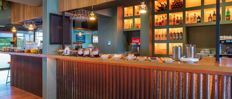 Zona de bar con mostrador de madera, estantes con botellas y un panel con la carta.