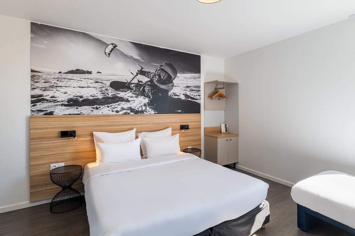A modern hotel room with a bed, bedside table, and a large wall mural.