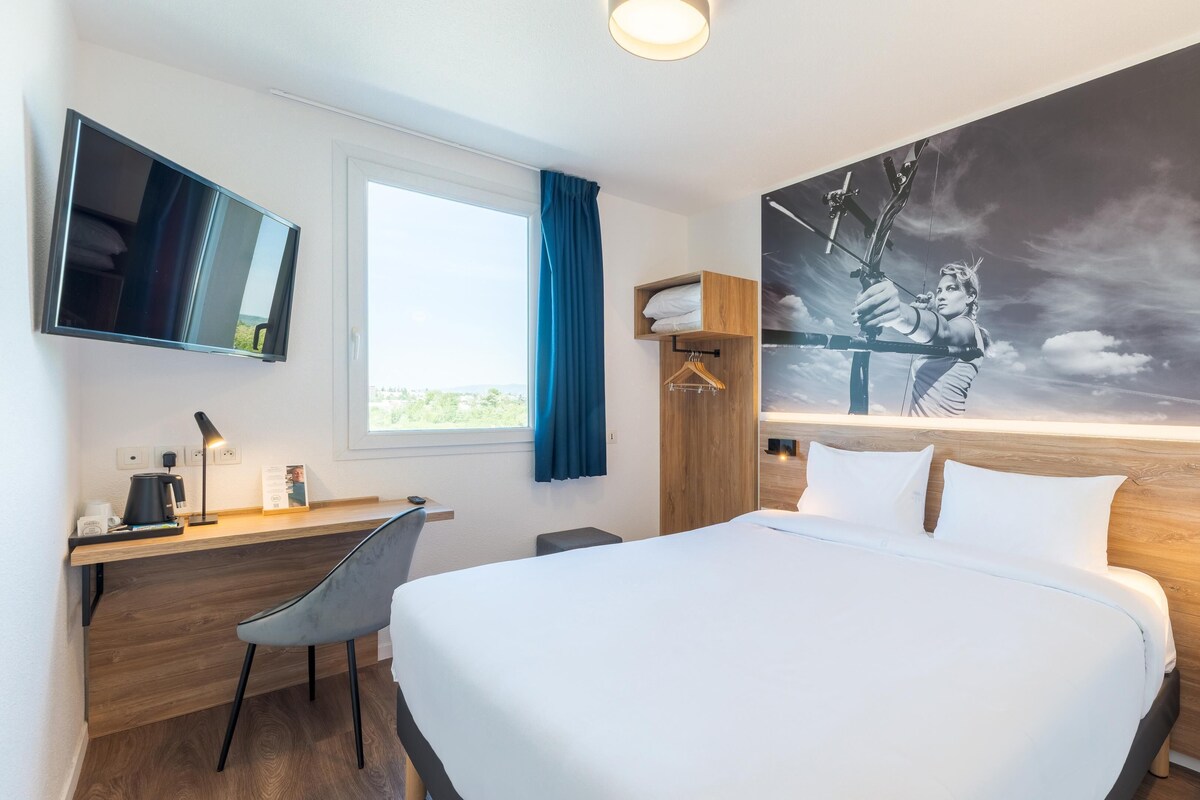 Una habitación de hotel moderna con cama, escritorio, silla y un gran mural en la pared.