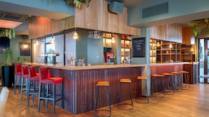 A bar area with a wooden counter, red bar stools, and shelves stocked with bottles. - Campanile PRIME - Lyon Meyzieu Eurexpo Arena Stadium (Meyzieu)