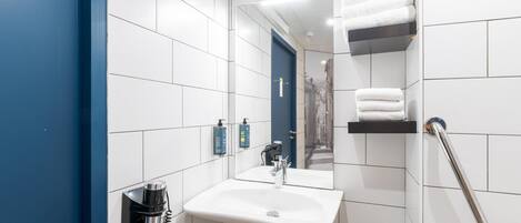 Un baño con baldosas blancas, una pared azul, un lavabo, un espejo y un perchero para toallas.