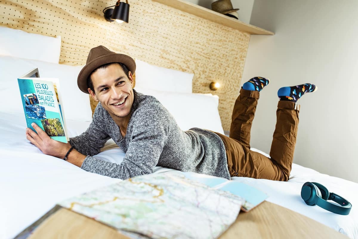 Una persona recostada en una cama con un libro, un mapa y audífonos.