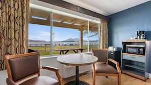A room with a table and chairs, a microwave, and a view of a bridge and mountains.