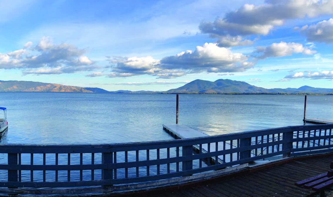 A wooden dock extending into calm water with mountains in the background.