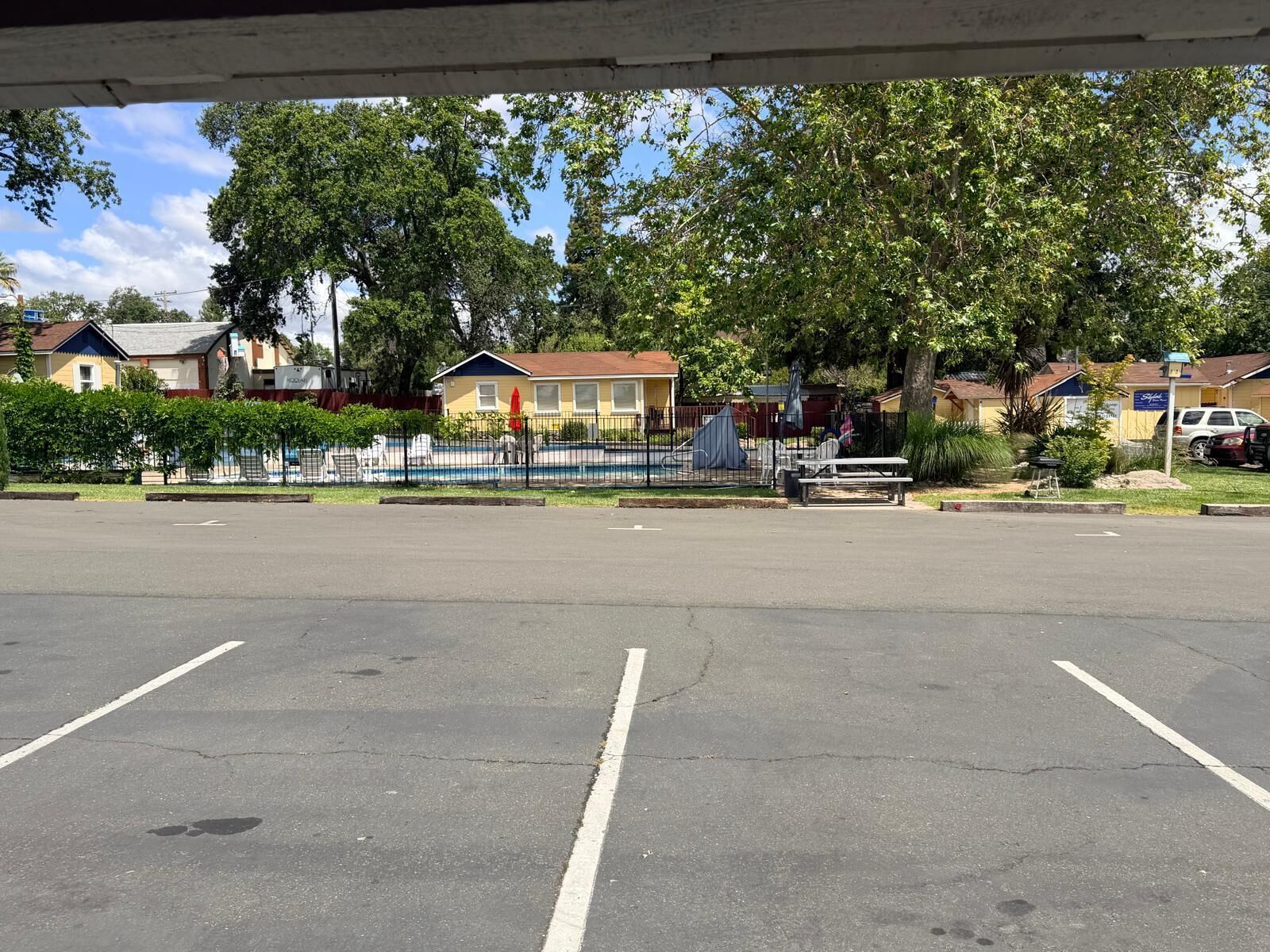 A parking lot with a fence, a picnic table, and houses in the background.