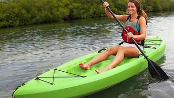 Eine Person paddelt mit einem grünen Kajak auf ruhigem Wasser, ein Paddel in der Hand, trägt eine Schwimmweste, Bäume im Hintergrund.