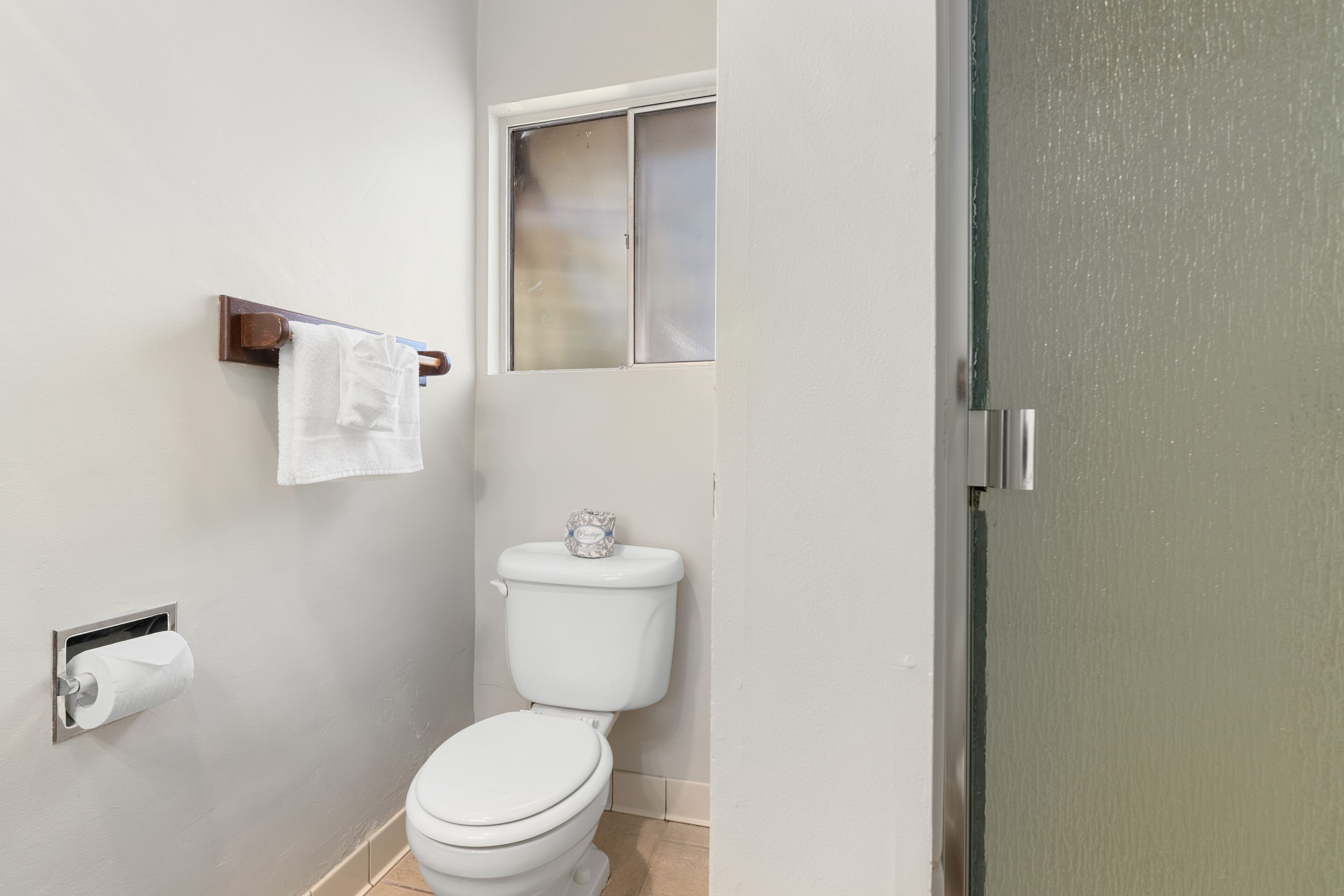 A bathroom with a toilet, a towel rack, and a window.