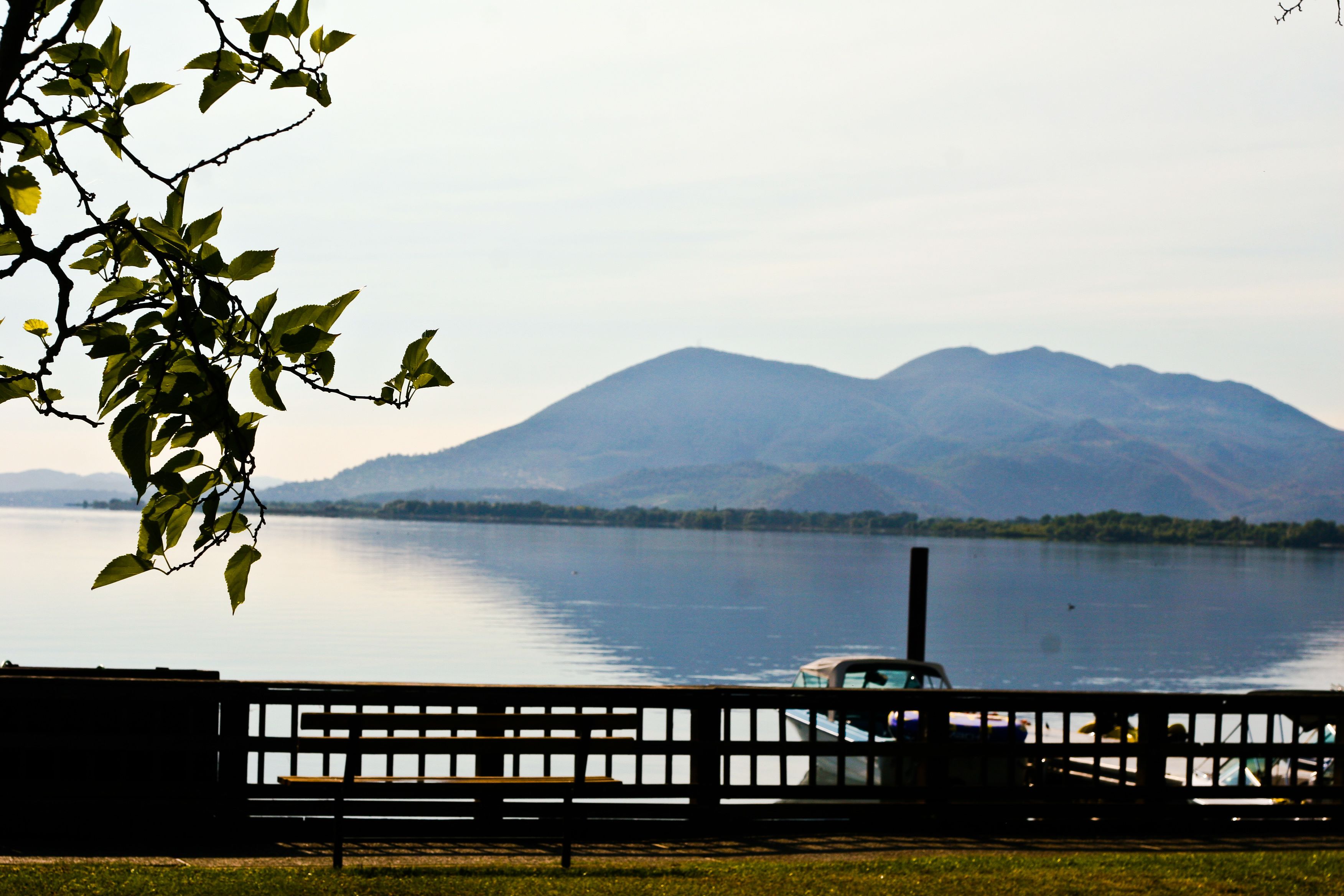 A lake with mountains in the background, a boat, and a bench in the foreground.